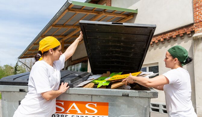 V.l.: Plamena Todorova und Andreea Dodoloi von der Bio-Backstube legen Pappkartons der Lieferanten in einen SAS-Container